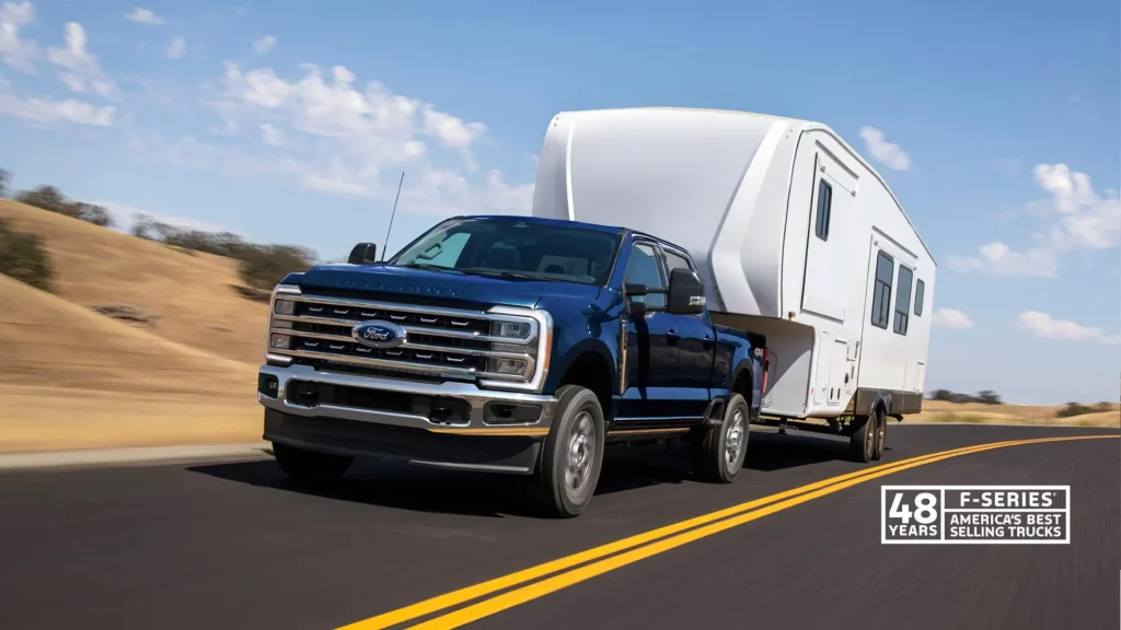 An F-250 towing an RV Travel Trailer on a road in a dry climate with a bright blue sky, dotted with clouds in the backdrop. There is a logo in the lower lefthand corner that says 48 years, F-Series, America's Best Selling Trucks.