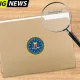 A wood background with a manila folder that has the FBI logo on the front and Grand Design's logo on the tab. In the upper lefthand corner is a bright green and black graphic stating "BREAKING NEWS" as a magnifying glass sit over the Grand Design logo on the folder.