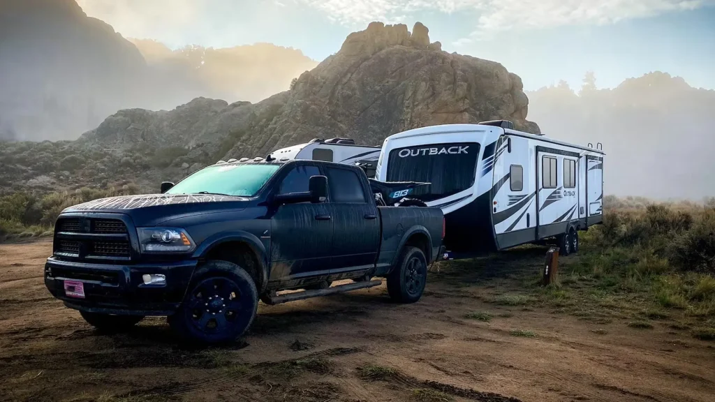 A keystone travel trailer being towed by a dodge Ram in a foggy humid climate as it sits in front of a rocky ridge.