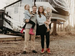 Nathan and Marissa from Less Junk, More Journey with their two children as they stand holding them on their hips in front of their RV.