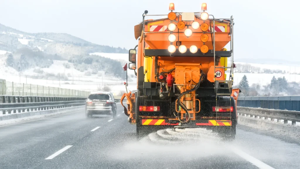 A salt truck dispersing salt on a highway in a snowy landscape. 