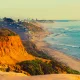 Encinitas Beach in southern California. This photo depicts a sepia toned photograph of bright blue waters and orange cliffs looking out to the ocean.