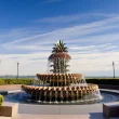 The infamous Pineapple Fountain in Charleston SC symmetrically displayed with shrubs and walkways around and beside it with a blue sky containing wispy clouds.