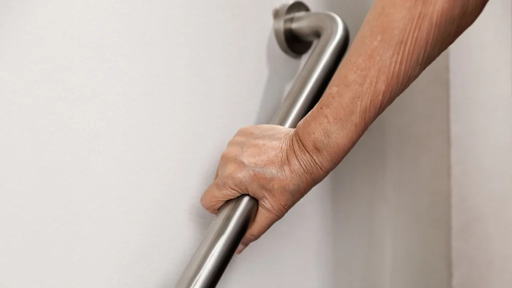 A close up photo of a hand holding onto a handrail agaist a white wall.