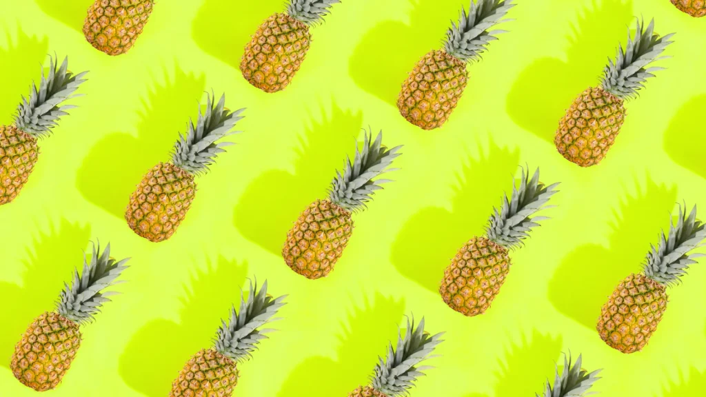 A neon yellow-green background with 14 pineapples laying over the top of it along with their shadows diagonally. 