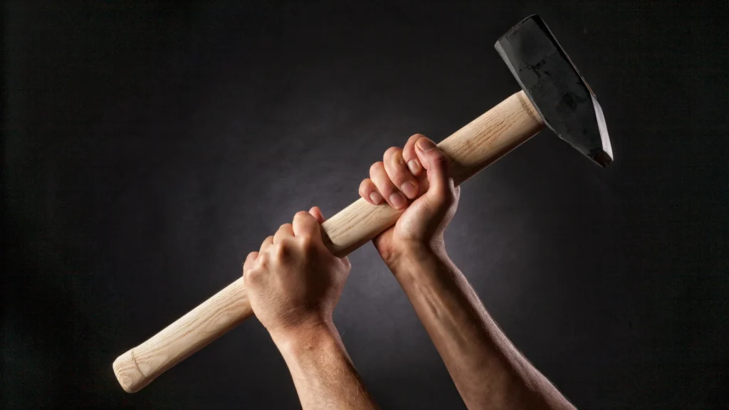 A closeup of a person's hands holding a sledgehammer against a black and grey bakcground.