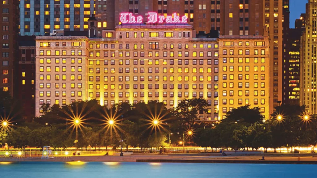 An image of the Drake Hotel at dusk with its signature neon sign lit up at the top in a pink-purple color.