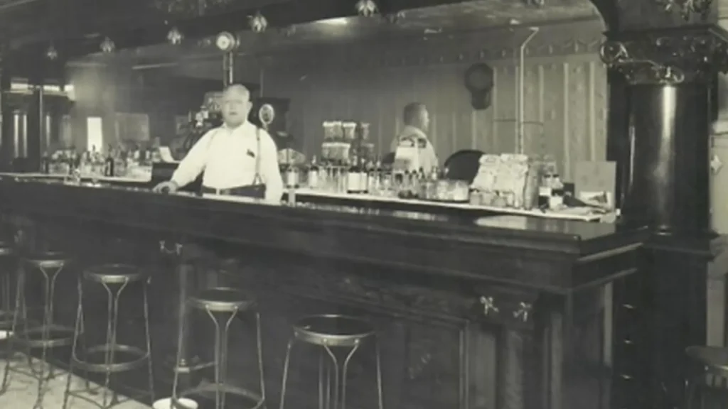 A vintage photo of the bar that used to be in the Great Escape Restaurant in the 1920's with the barkeep standing behind it. 