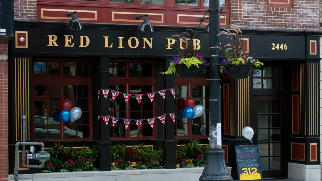 The outside of the Red Lion Pub is currently adorned with red, white, and blue balloons, British flag banners, and a chalkboard sign sitting out front. 