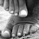 An up close black and white photo of feet in the sand on a beach as one rubs the other.