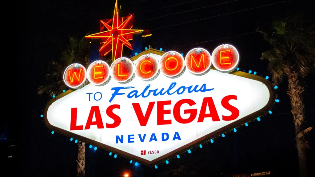 A "Welcome to Fabulous Las Vegas Nevada" neon sign in red, blue, yellow, and white. There's a neon star at the top and a palm in view on the righthand side. It's dark outside.