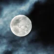 A photo of a full moon with clouds partially covering the night sky.