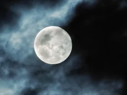 A photo of a full moon with clouds partially covering the night sky.