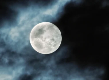 A photo of a full moon with clouds partially covering the night sky.