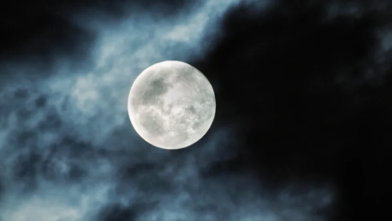 A photo of a full moon with clouds partially covering the night sky.