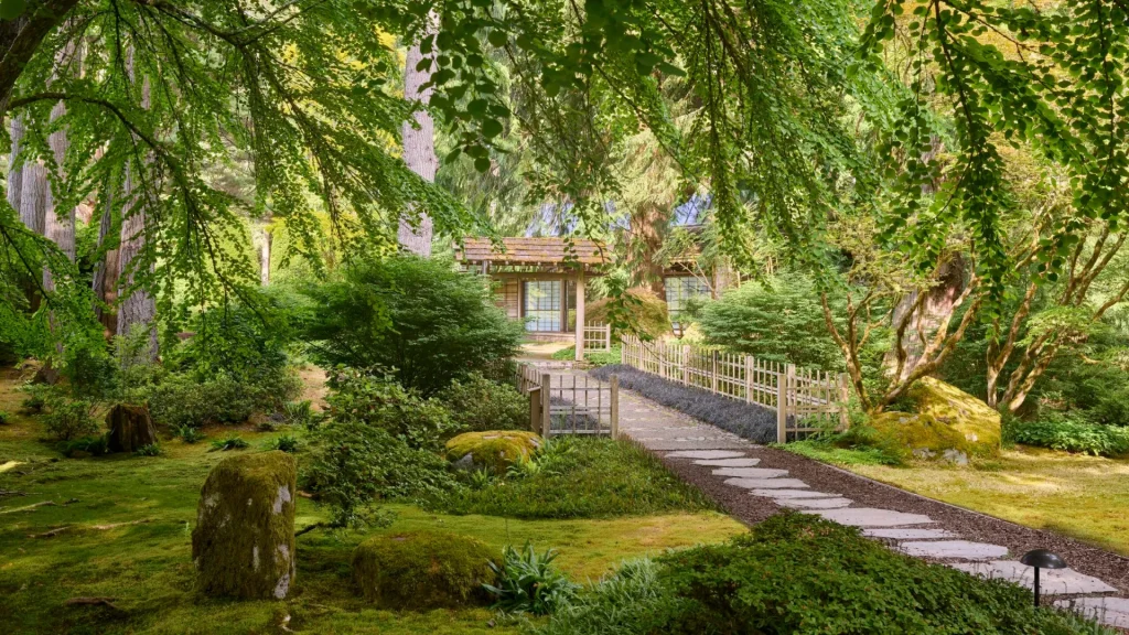 An image of a path trailing up to a wooden structure in the Bloedel Reserve. There are trees and stones covered in moss in this verdant photo.