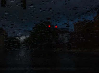 A photo from the inside of a vehicle on a dark rainy night as it stop at a red light.