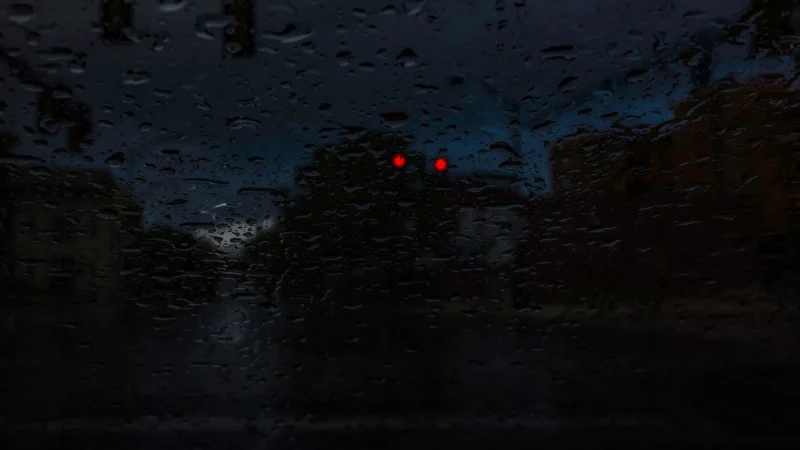A photo from the inside of a vehicle on a dark rainy night as it stop at a red light.