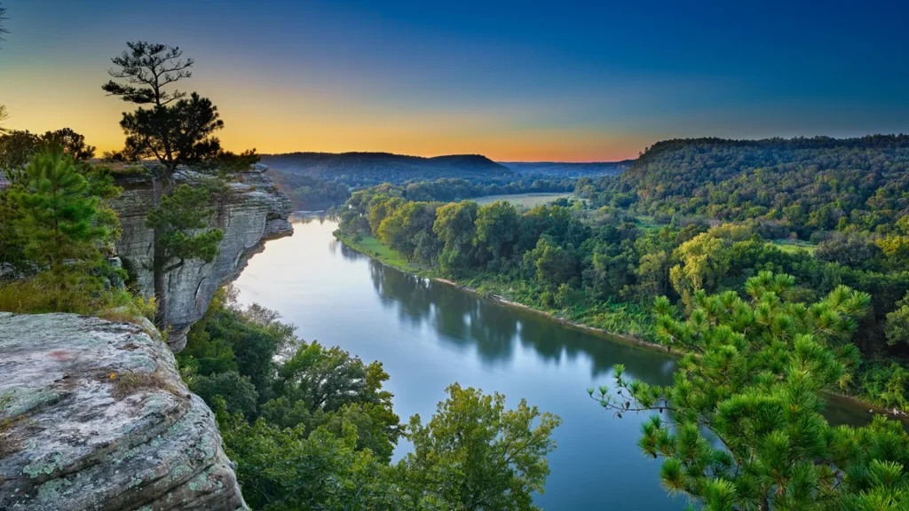 A sunset photo of the White River in Arkansas as the dense foliage reflects in the still water.