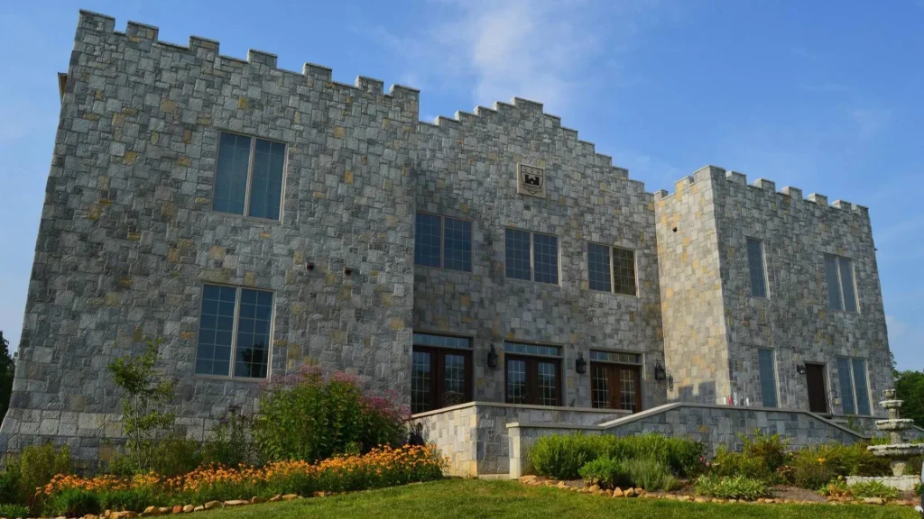 The Clayshire Castle in Indiana, a stone castle, simple in structure, with large windows and three sets of doors in the front. The lawn is meticulously manicured around it. 