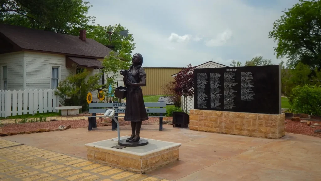 A bronzed statue of Dorothy holding Toto in a brick-lined landscape.