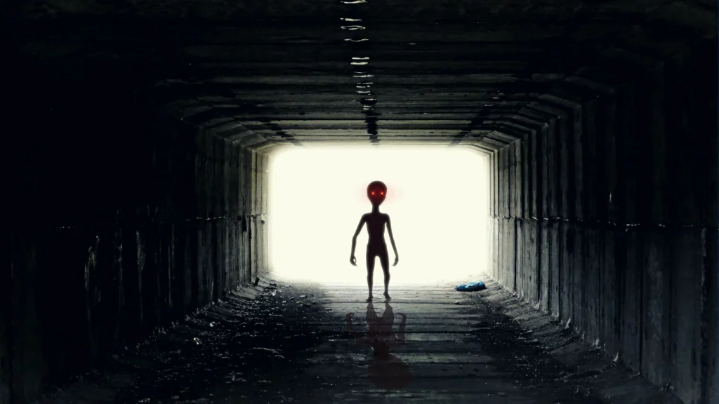 A representation of the Dover Demon, looking similar to imagined images of aliens with red glowing eyes, as it stalks down a dark tunnel.