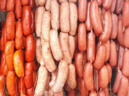 Strings of different types of sausages hanging side-by-side ranging in colors of red, orange, and pinks.