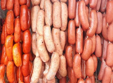 Strings of different types of sausages hanging side-by-side ranging in colors of red, orange, and pinks.