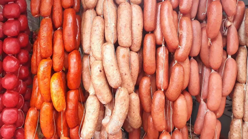 Strings of different types of sausages hanging side-by-side ranging in colors of red, orange, and pinks.
