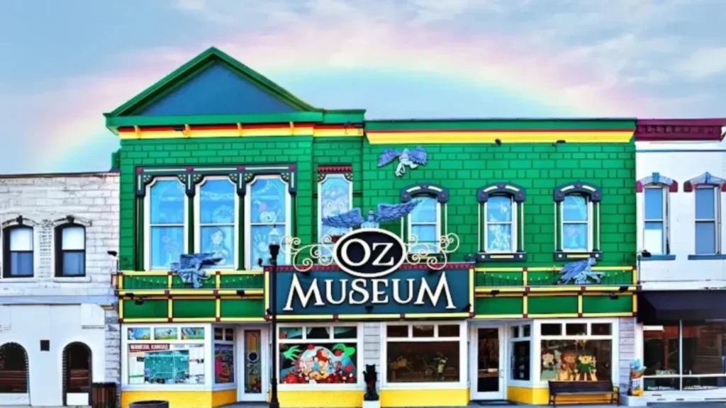 An image of the Oz Museum's storefront in its signature emerald green. There is a faint rainbow in the sky behind the building.